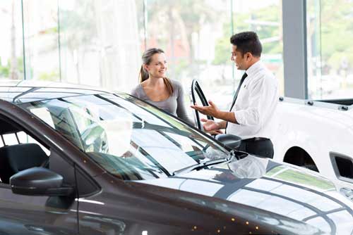 Woman negotiating car price at dealership after college graduation.