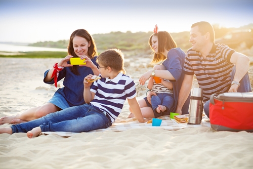 mom and dad sitting on beach with son and daughter smiling at how much money they saved traveling there following these tips