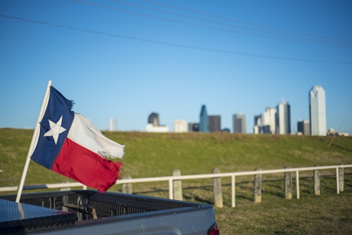 texas state flag waving in the wind from back of pickup truck protected by comprehensive car insurance white picket fence clear blue skies