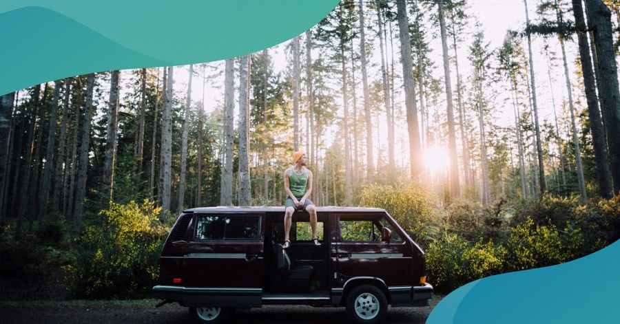 man sitting on top of his van in the middle of the woods