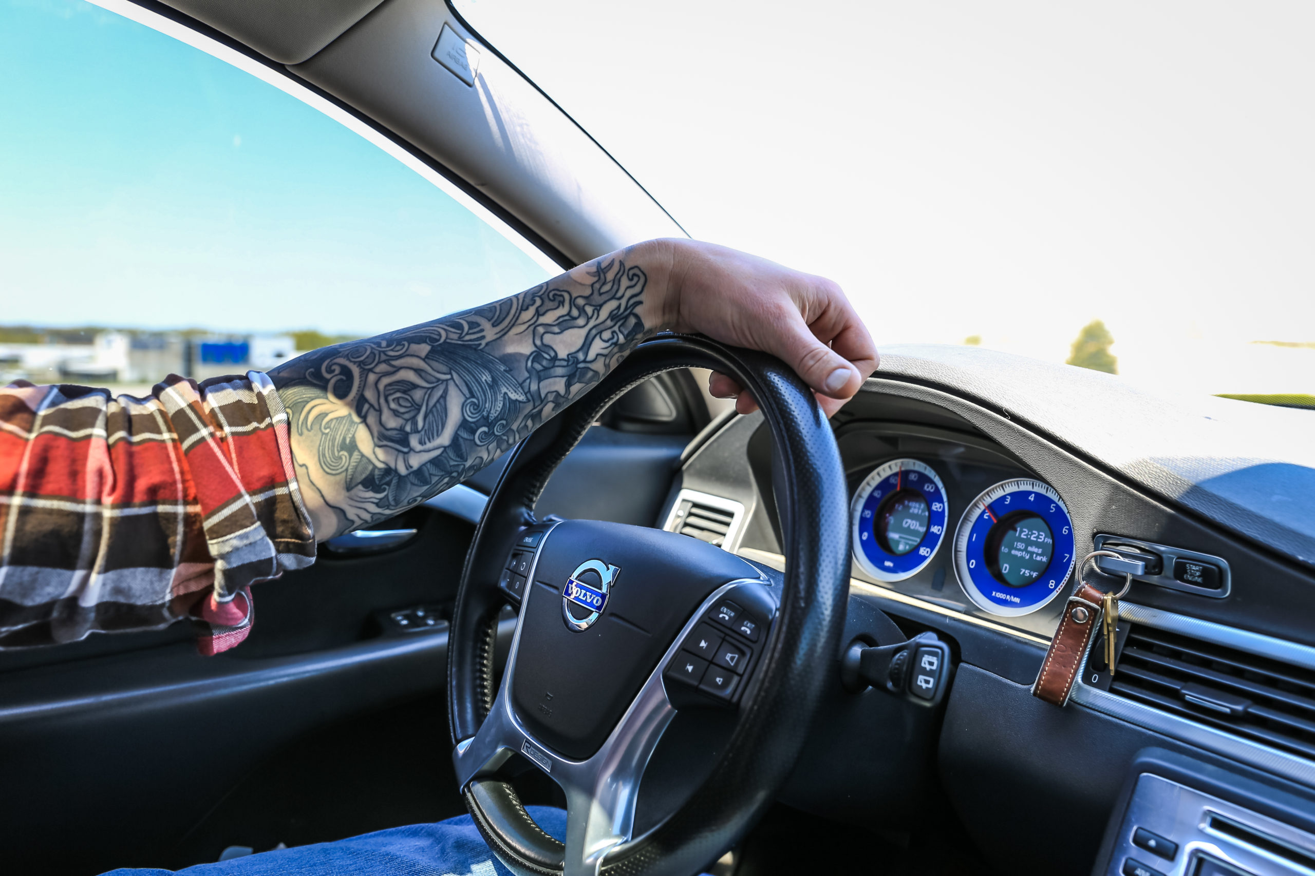 man's tattooed arm on steering wheel practicing good ergonomics