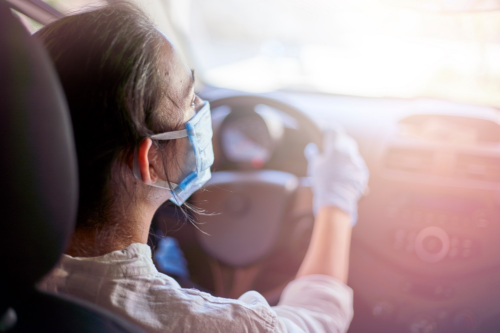 A woman in a surgical mask and gloves driving avoiding COVID-19