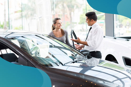 A young woman talks to a man at a car dealership.